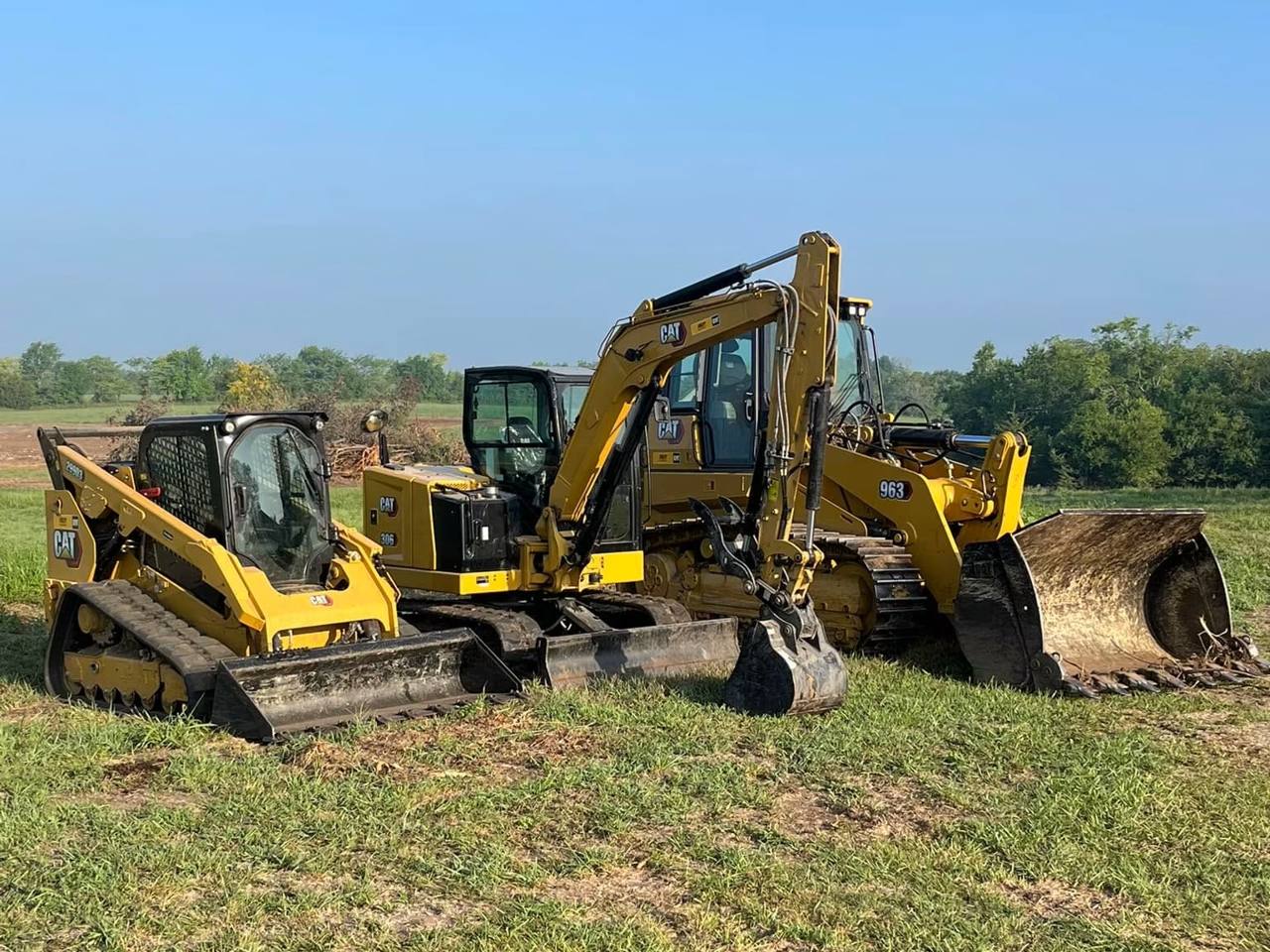 Caterpillar track loader, mini excavator and wheel loader lined up in a field