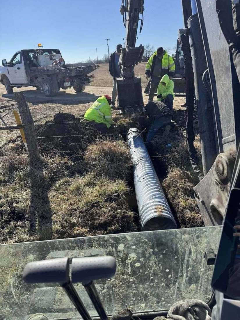 Crew installing underground drainage pipe on a fence line